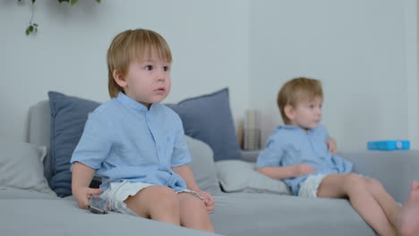 Two-boys,-4-and-2-years-old,-are-watching-TV-sitting-on-the-couch.-An-exciting-TV-show.-View-cartoons